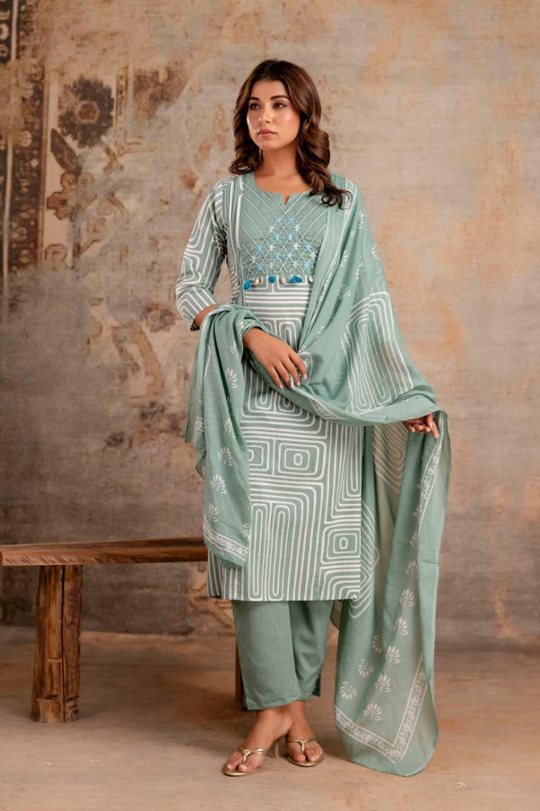 Woman wearing a light green traditional outfit with a matching dupatta against a textured wall.