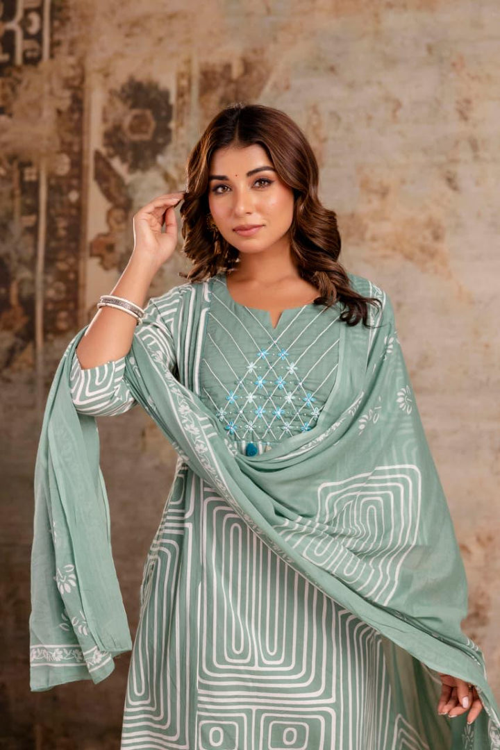 Woman wearing a light green traditional outfit with a matching dupatta against a textured wall background