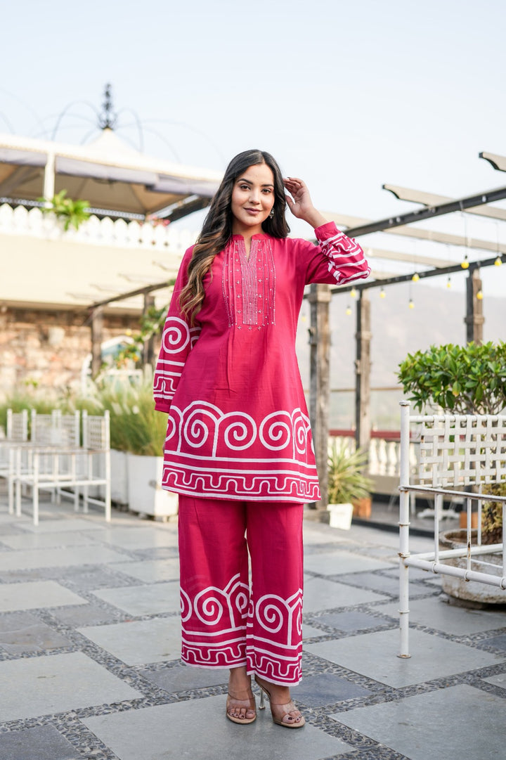 Woman in a red traditional outfit with white patterns standing on a rooftop patio.