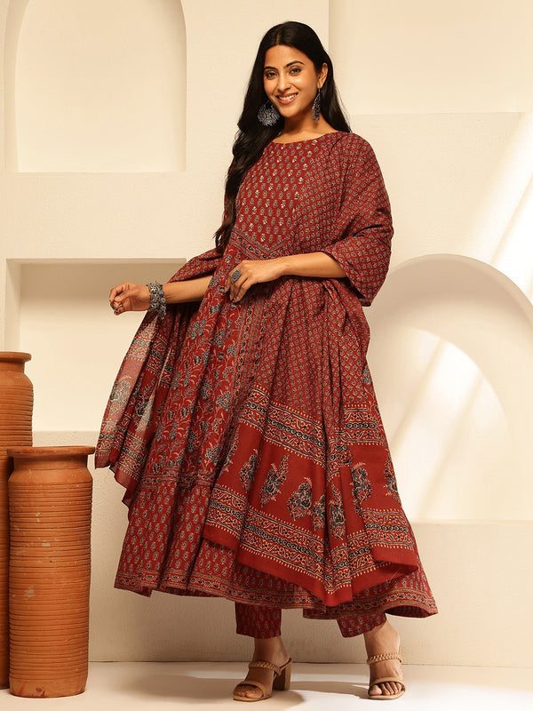 Woman wearing a red patterned dress standing against a white wall with clay pots.