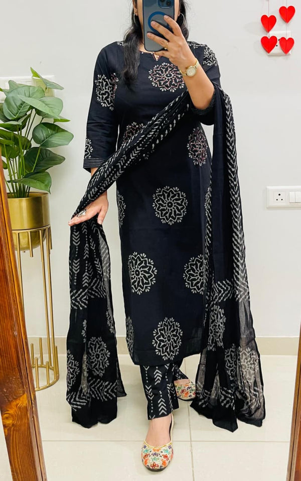 Person wearing a black traditional outfit with white patterns in a room.