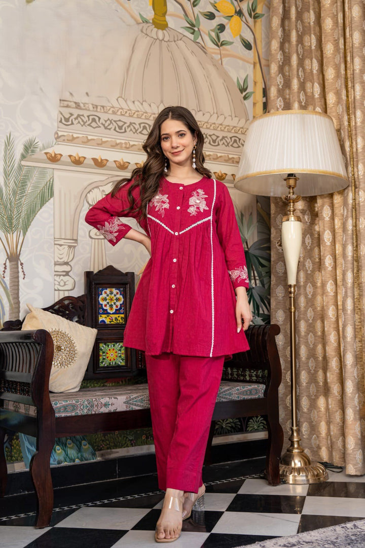 Woman in a pink traditional outfit standing in a decorated room with lamps and furniture.