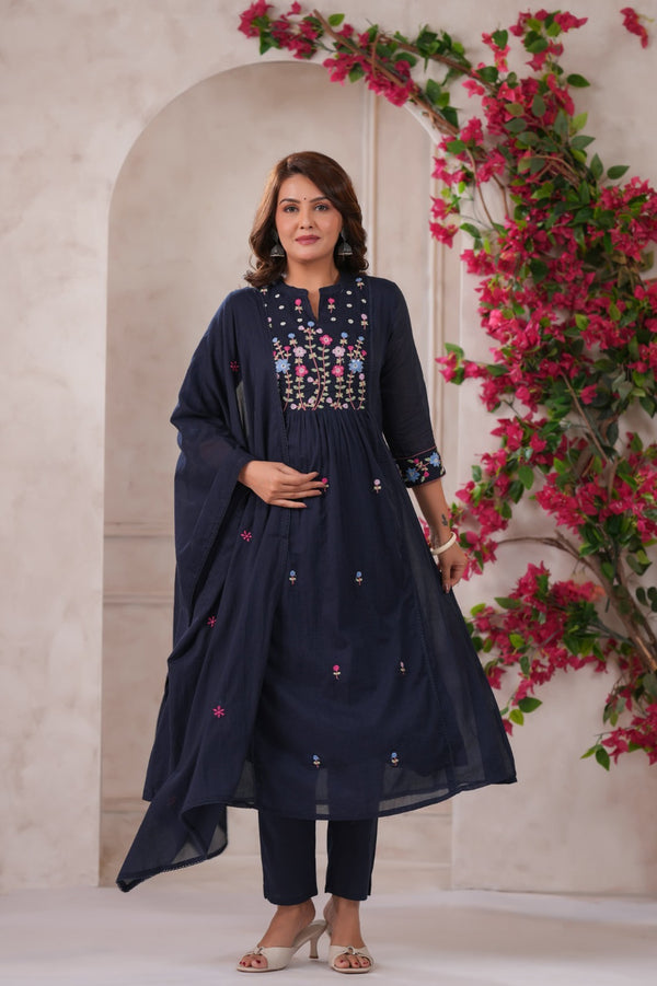 A woman wearing a navy blue traditional outfit with floral embroidery against a floral backdrop.