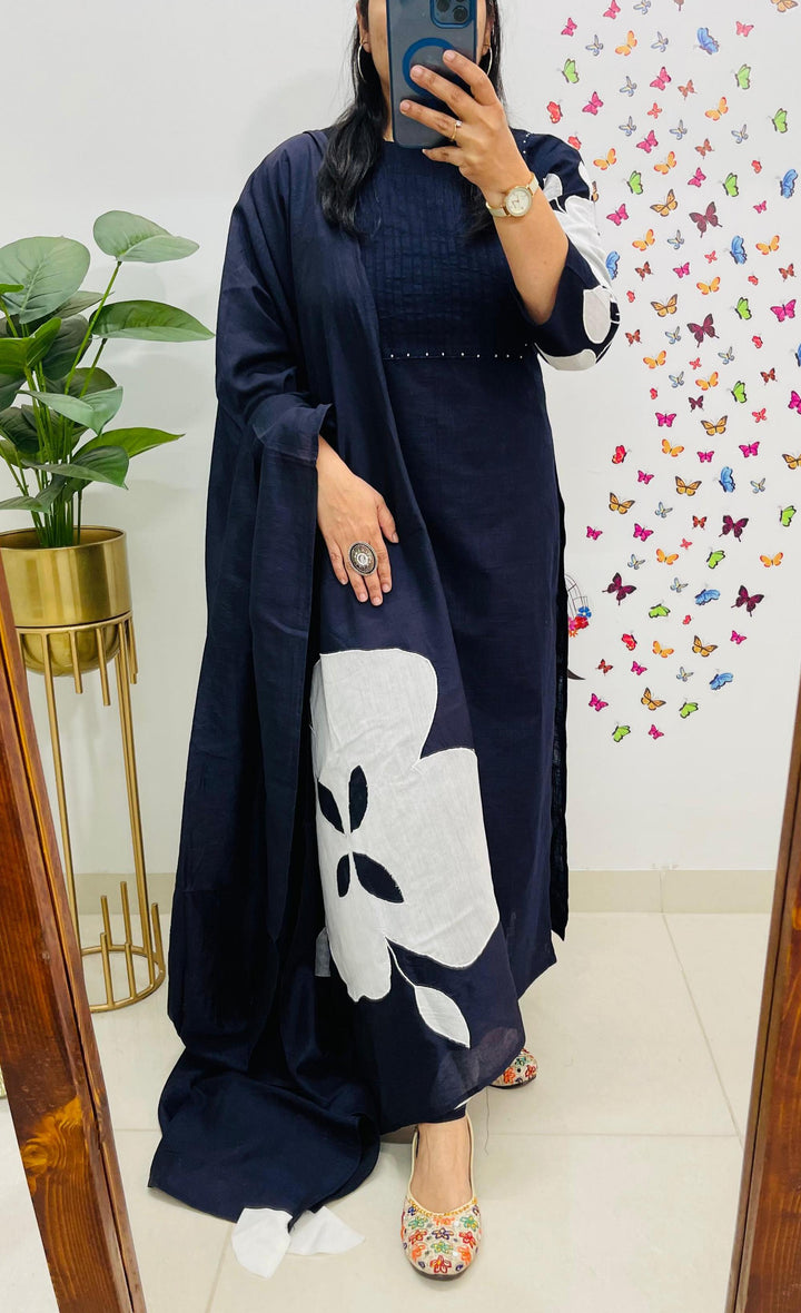 Person wearing a navy blue dress with a white floral design, standing in front of a colorful butterfly-patterned wall.