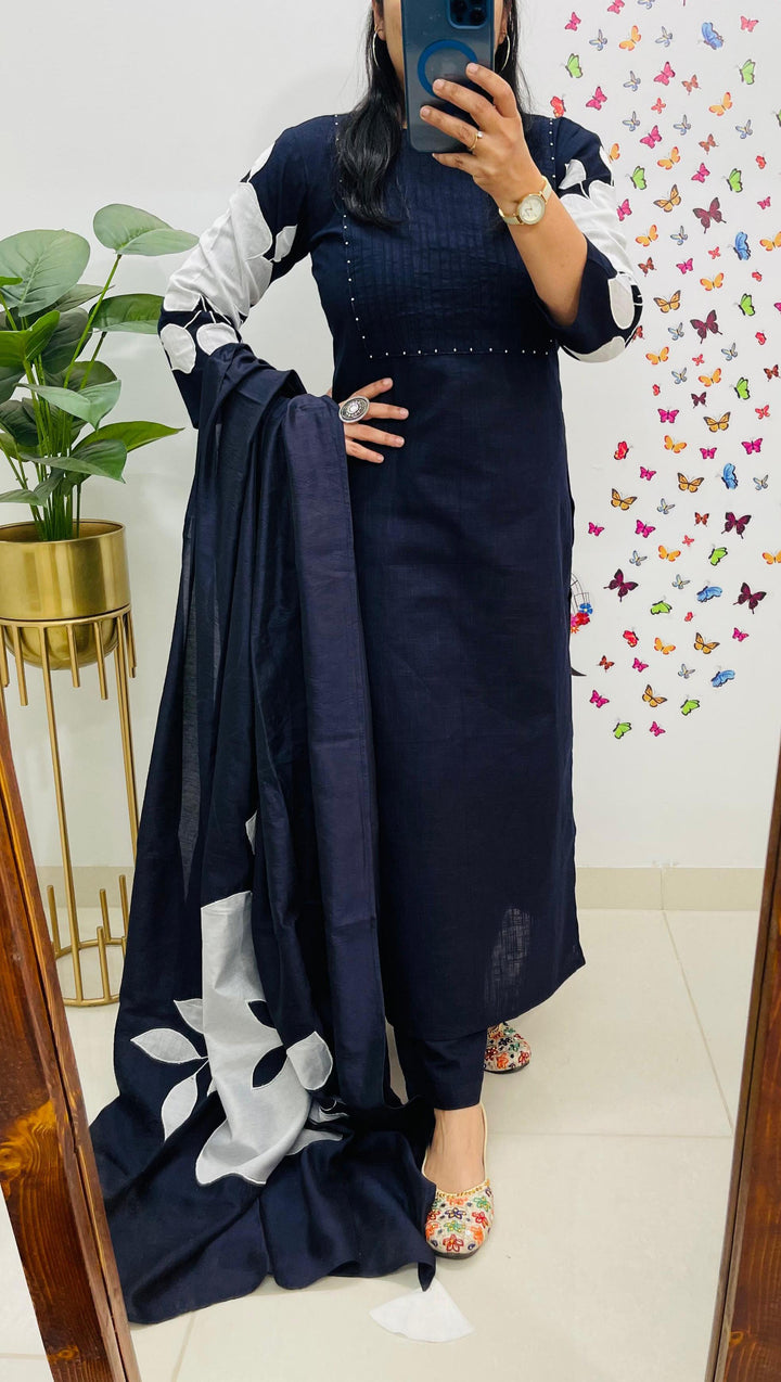 Person holding a navy blue outfit with white patterns in front of a mirror.