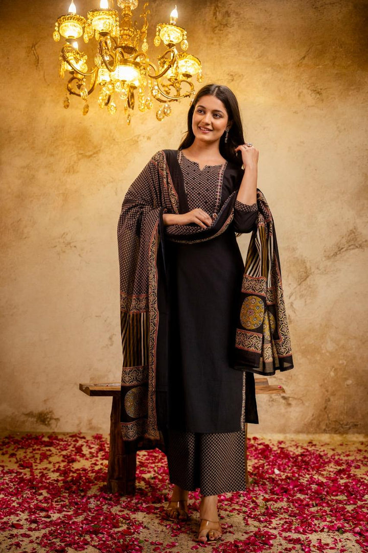 Woman in traditional attire standing in a room with a chandelier and floral carpet.